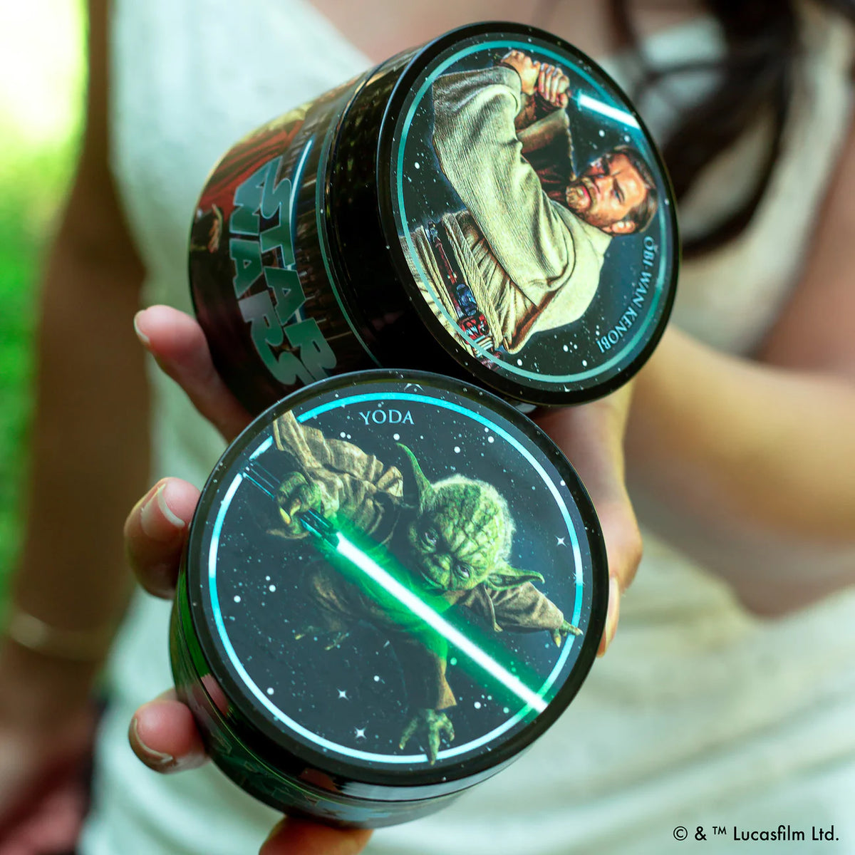 Two Suavecito Pomade containers with Star Wars-themed designs, featuring Yoda and another character, held by a person.