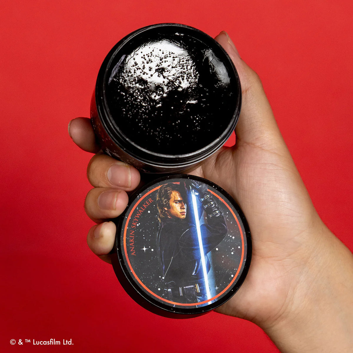 Hand holding a black container with a character from 'Star Wars' on a red background